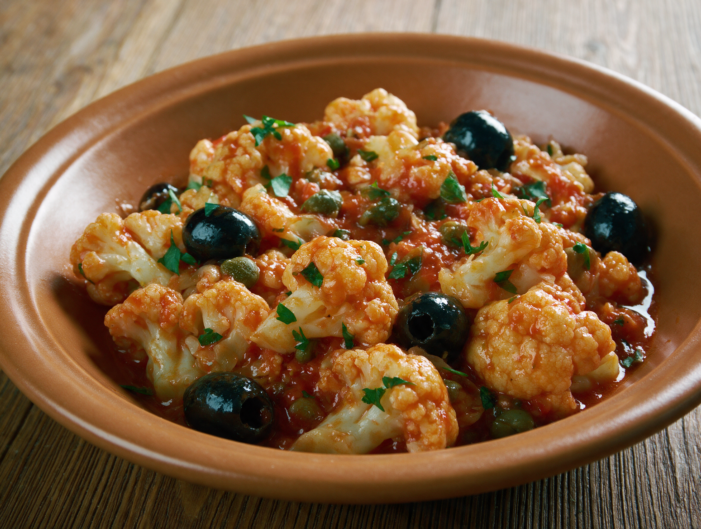 Cavolfiore affogato in a shallow bowl, cauliflower florets glazed in tomato-wine sauce with olives and parsley on top.