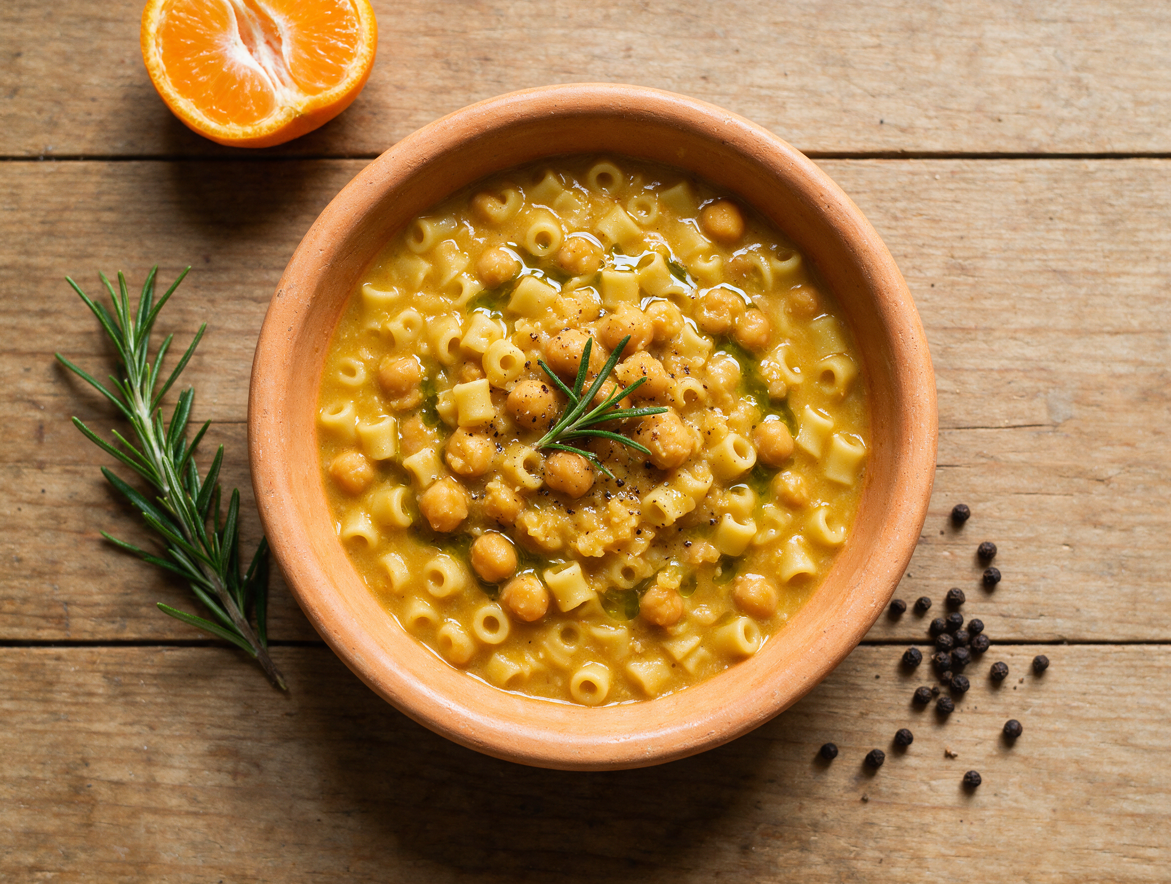 Overhead view of pasta e ceci alla romana in a rustic bowl with tubetti pasta, chickpeas, and a rosemary sprig.