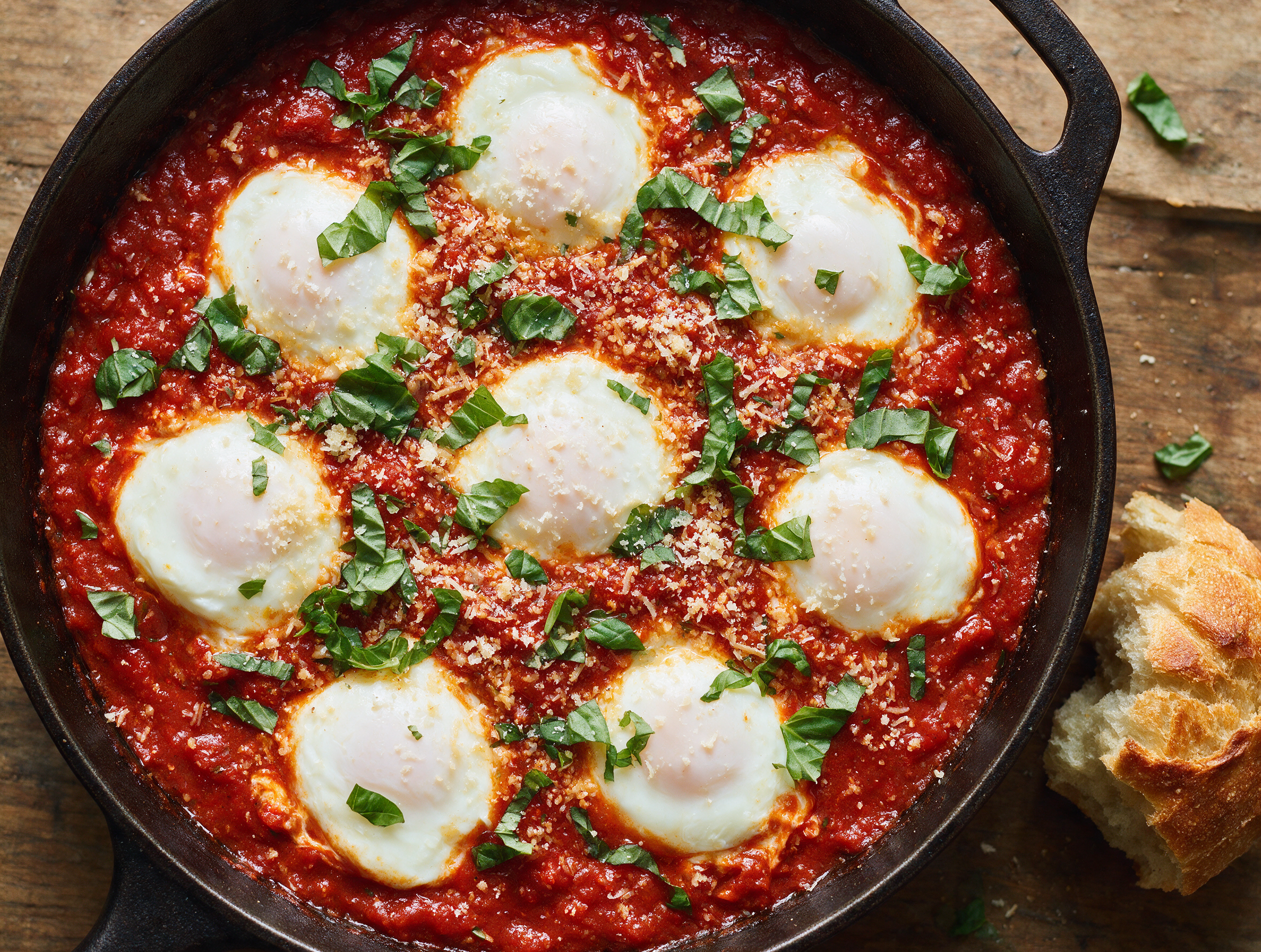 Overhead view of uova in purgatorio, poached eggs in glossy red chile tomato sauce, basil scattered on top