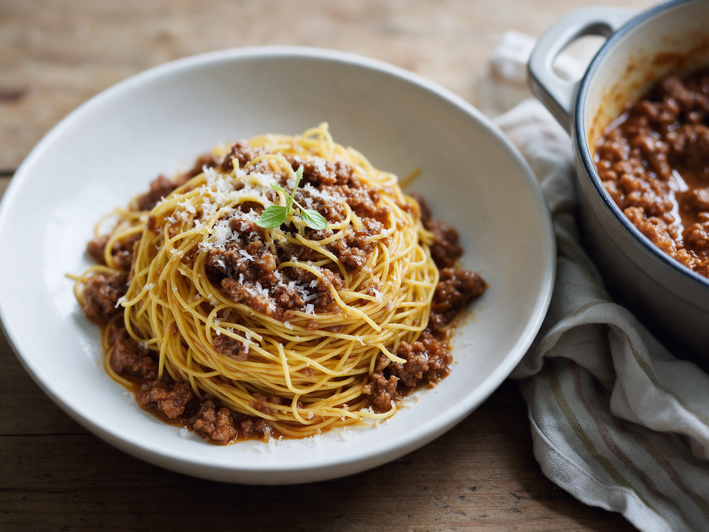 Overhead view of a nest of golden egg pasta with beef and pork ragù and grated Parmigiano in a white bowl