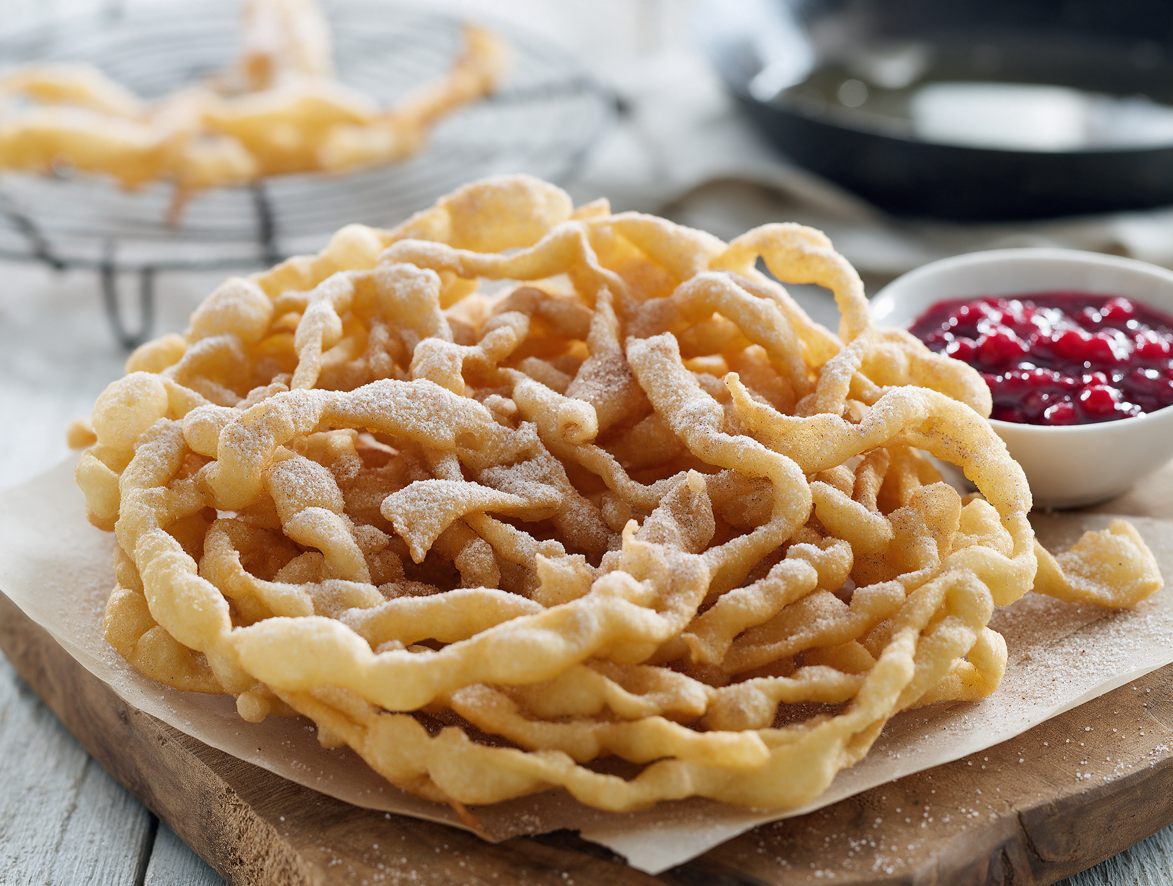 Golden lacy fried Strauben dusted with cinnamon sugar beside a bowl of lingonberry jam