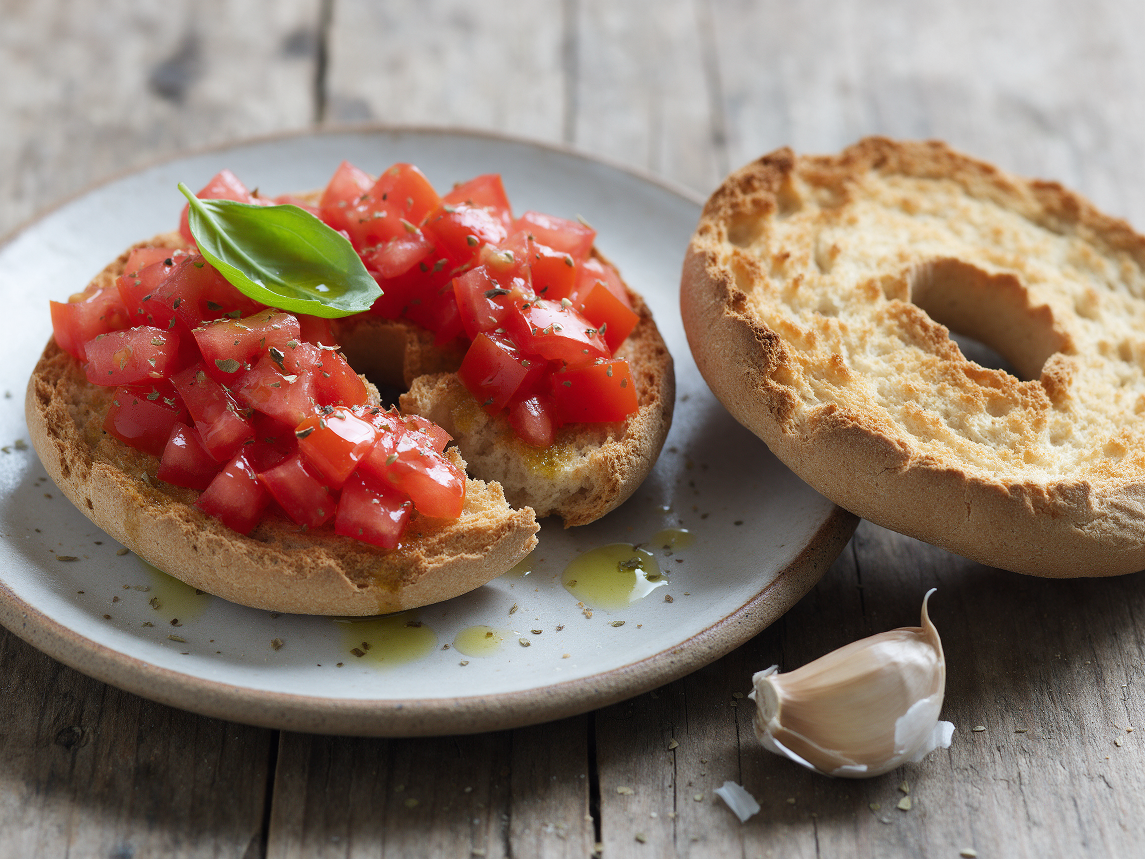 Friselle topped with diced tomatoes, olive oil, and oregano on a ceramic plate, shot at 45 degrees